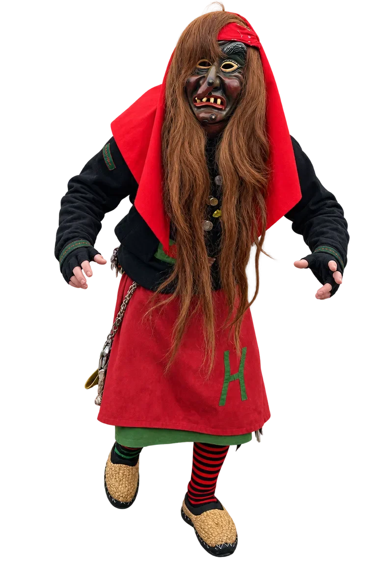 Huzler Hexa im traditionellen Häs mit Maske und langen rötlichen Haaren.